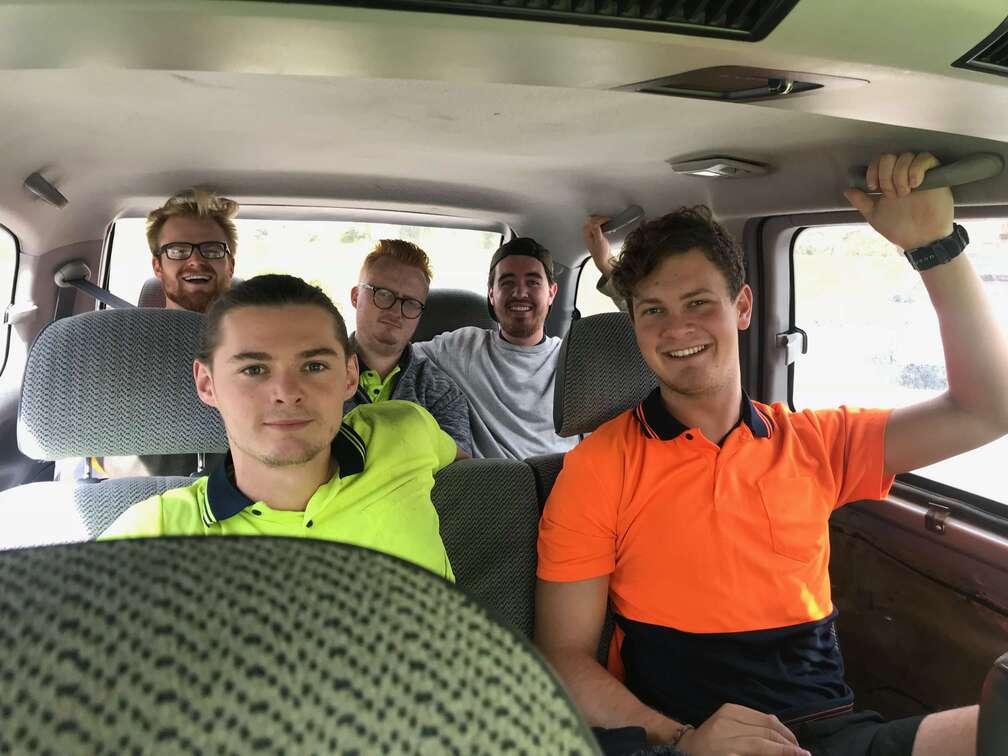 Six backpackers in hi-vis work shirts packed into a people carrier