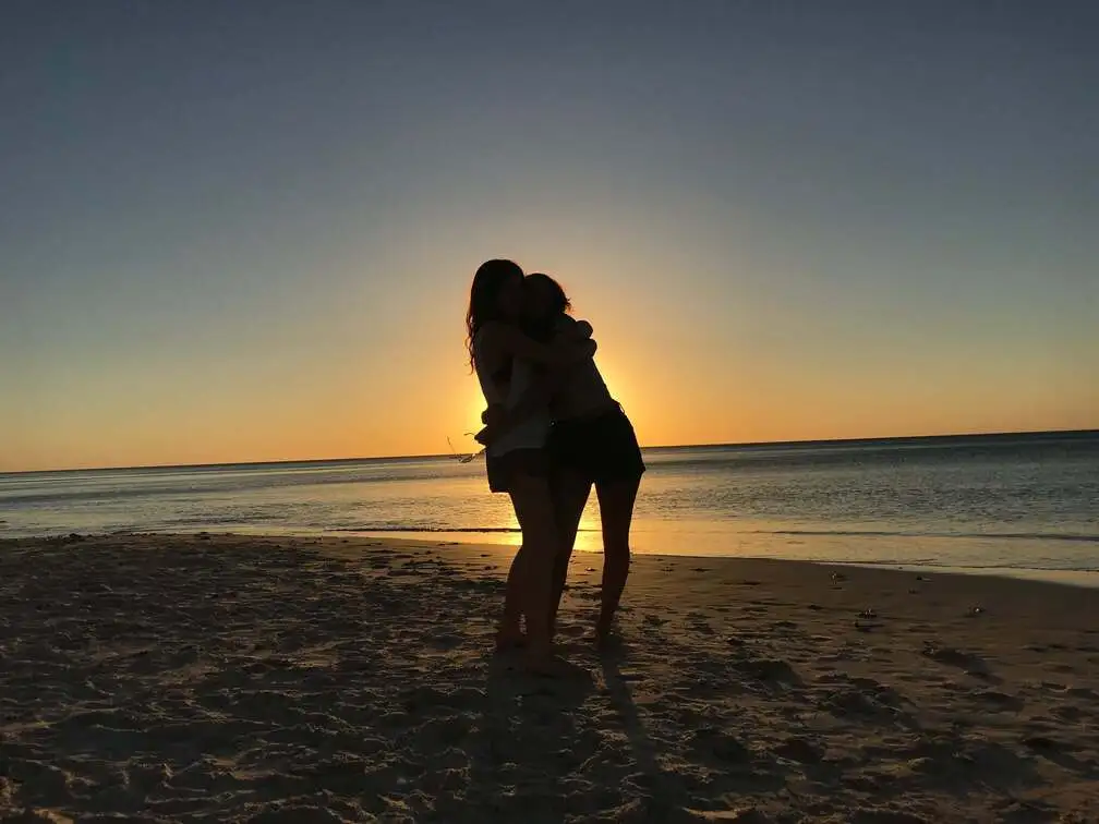 Two backpackers embracing on a beach at sunset